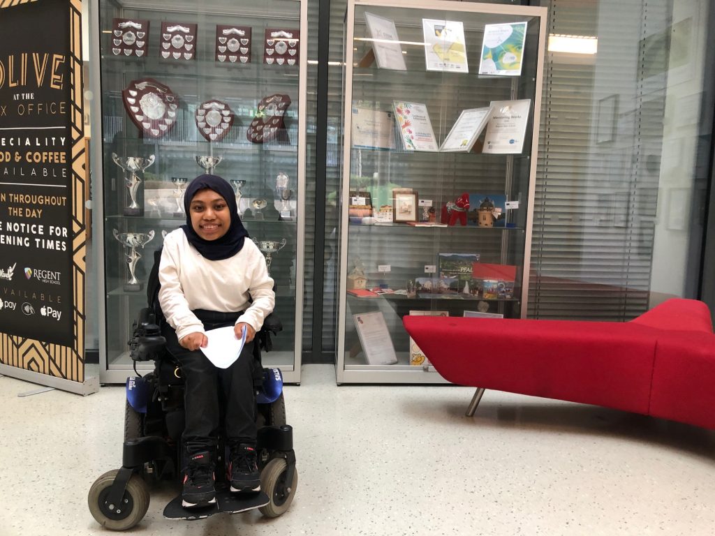 Woman in wheelchair next to awards cabinet in Regent High School on A Level results day