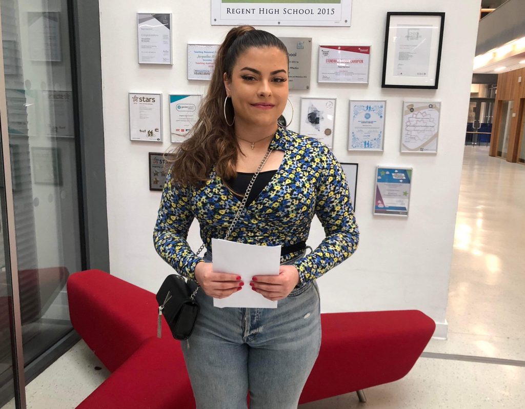 Female pupil holding white piece of a4 paper with A Level results on 